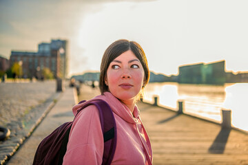 Portrait of a young beautiful brunette girl who stands on the canal embankment at sunset....