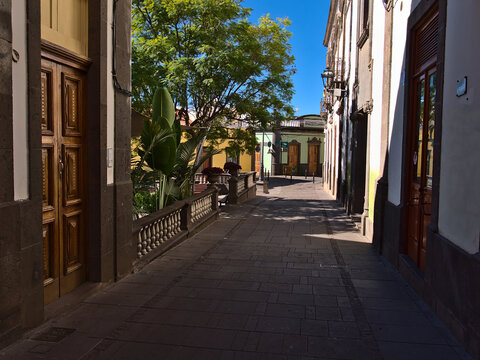 View of empty narrow alley in the historic center of Arucas on island Gran Canaria, Canary Islands, Spain on sunny day with old buildings and park.