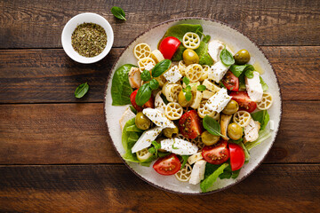 Chicken Caprese pasta salad with mozzarella cheese, olives, tomato and fresh basil. Top view, flat lay