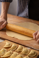 Dough rolling process. A man in a plaid shirt rolls out dough for dumplings with a rolling pin. In the foreground dumplings with cottage cheese on a cutting board