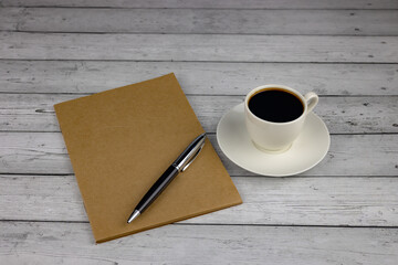 A cup of coffee, a notebook and a pen on a wooden table. The concept of planning a day over a cup of coffee. Close-up