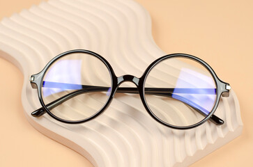 Stylish round glasses for vision on a wavy beige podium