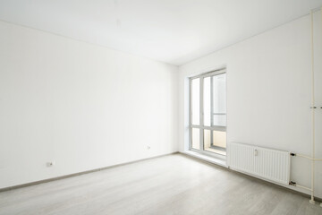 Empty room with laminate flooring and newly painted white wall in background.