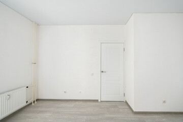 Empty room with laminate flooring and newly painted white wall in background.