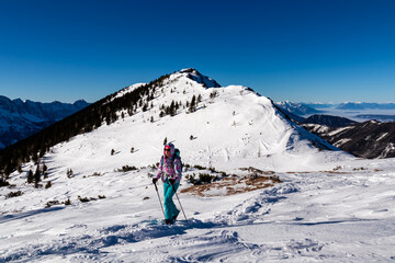 Fototapeta na wymiar Active woman snow shoe hiking on a trail with scenic view from Hochobir on mountain peaks of Karawanks in Carinthia, Austria. Ski tour. Sunny winter wonderland day. Freedom. Valley covered with clouds