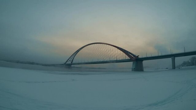 in the early morning a blizzard with snow sweeps and the sun slowly illuminates the transport bridge in siberia