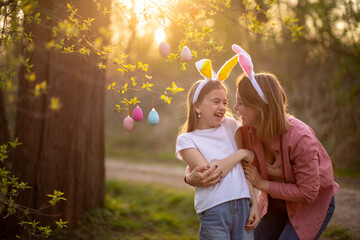 beautiful and happy mom and daughter in bunny ears decorate the tree with easter eggs. happy family...