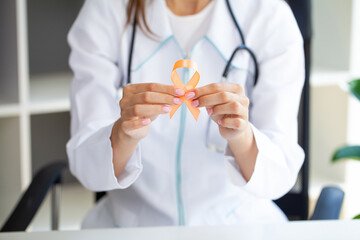 Close up of a doctor holding and showing orange awareness ribbon in her hands