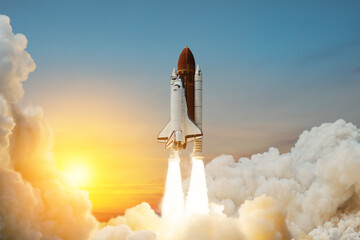 Spaceship lift off. Space shuttle with smoke and blast takes off into space on a background of sunset. Successful start of a space mission. Travel to Mars. Elements of this image furnished by NASA. - obrazy, fototapety, plakaty