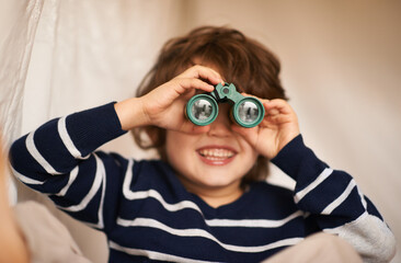 Lets see what mischief I can get up to today. Shot of an adorable little boy playing with a pair of binoculars.