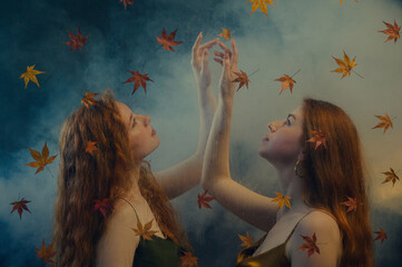 Two beautiful redhead freckled women with long natural curly hair posing in smoke, darkness and...