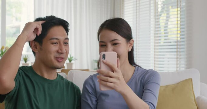 Asia people young couple relax leisure good easy time at cozy sofa home enjoy fun play phone trending filter effect selfie challenge in social media app IG reel tiktok viral video story photo shoot.