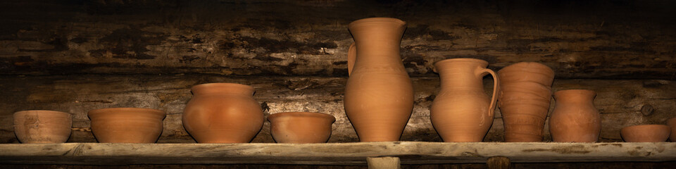 earthenware stands in a row on a rough wooden shelf against a log wall. simple panoramic still life in rustic style. pottery shop