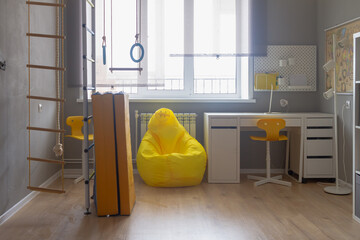 The interior of the room of a boy or girl of schoolchildren with sports equipment, a gymnastic Swedish wall, a yellow armchair with gray walls in light white shades