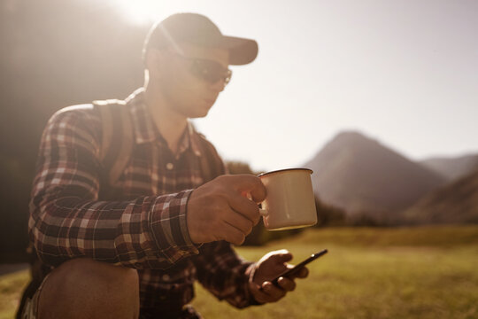 person holding mug and using smart phone in the mountains