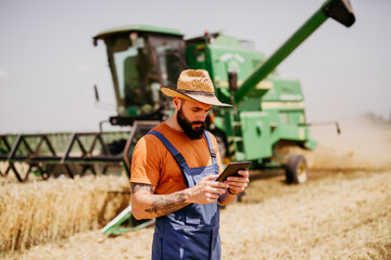 Young agronomist inspecting wheat field and using tablet computer.
