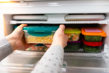 Woman taking containers with frozen corn out from freezer.