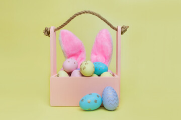 Wooden basket with colored eggs and pink rabbit ears. Easter concept