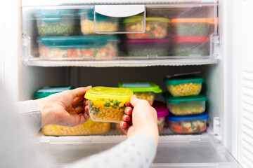 Woman taking containers with frozen peas and corn out from freezer.