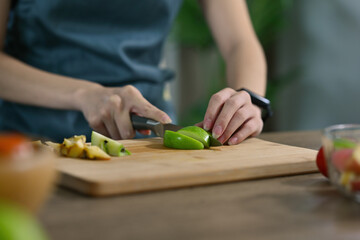 Cropped view young woman's hands chopping green apple and fruits preparing a meal on a wooden cut board, for food, health and cooking concept.
