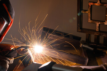 A male welder works at home with a semi-automatic welding machine, with golden sparks of steel...