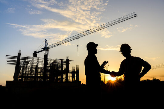 silhouettes of construction engineers or managers and construction workers on a construction site shake hands to agree on a work plan Design projects of houses and industrial buildings