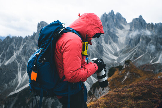 Photographer with red softshell jacket, backpack and radio station checking photos while hiking in the mountains in cold weather. Hiker using digital camera while trekking mountain trail