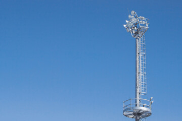 High metal mast with spotlights against a clear sky.