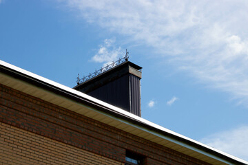 A roof with a chimney on the background of a blue summer sky.