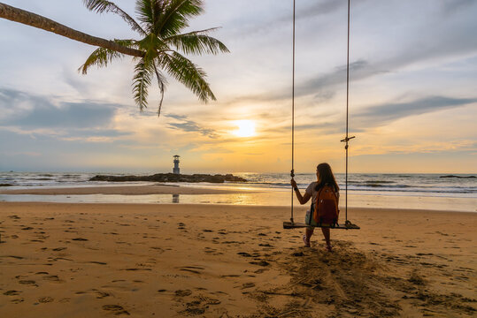 Single woman sitting on a swing enjoying sunset view at sea beach.Travel and summer vacation concept image.