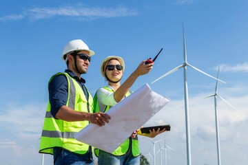 Asian man and woman engineers working on site in wind turbine on the background. Young people engineers working at renewable energy farm