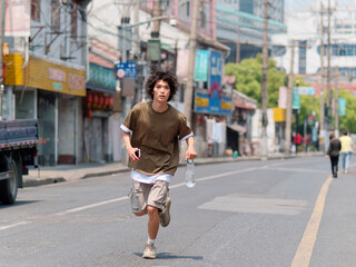 Portrait of handsome Chinese young man with black curly hair in brown T-shirt and pants running on...