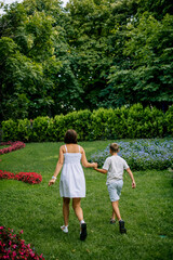 Obraz premium Smiling mother and son are walking in the park together in summer in light clothes. Soft sunset light.