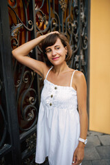 Beautiful brunette young woman in a beautiful white summer dress walks and poses in the summer in the city.
