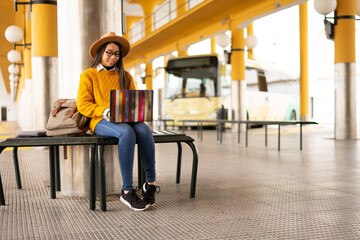 Chinese woman sitting in a bus station bench working with her laptop - obrazy, fototapety, plakaty