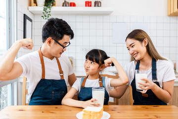 Asian  family enjoying breakfast at cozy kitchen, little girl daughter sitting on table, drinking...