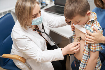 Female doctor examining child with stethoscope in clinic