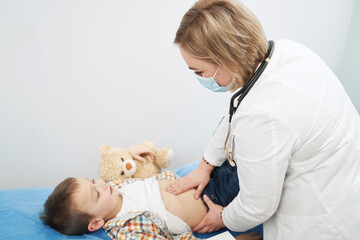 Female pediatrician examining child abdomen in clinic - obrazy, fototapety, plakaty