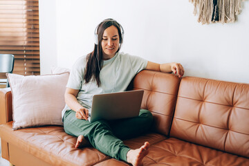 Young brunette woman freelancer working from home on a laptop while sitting on the couch.