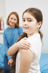 Little girl showing arm after getting vaccine injection in clinic