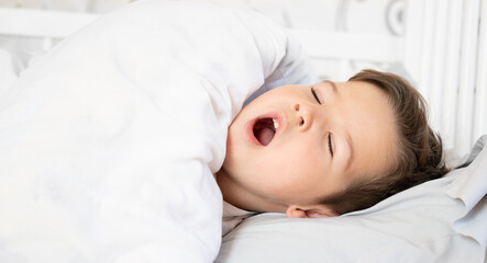 Portrait of a cute little boy who yawns in bed early in the morning 