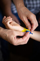 Hands of a child and an adult. Ribbon on hand. Flag of Ukraine. Support