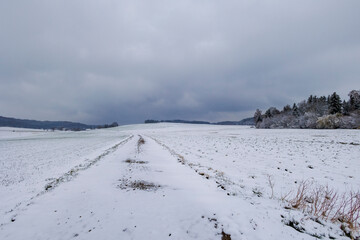 snowy field path with cloudy sky in Schmuttertal biotope near the village of Gablingen near Augsburg in Bavaria, Germany