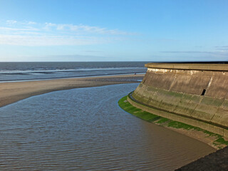 view of the concrete seawall in the cliffs area blackpool with the beach and incoming tide in sunlight with the outs wall of the old boat pool