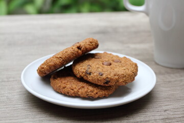 Three homemade sweet brown sugar cookies on white plate. Blur background of white glass and plants.