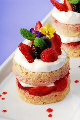 cake or sponge cake with red berries and edible flowers layered with whipped cream on lilac background, summer cake