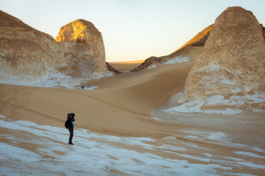 A tourist photographs sandstone formations in the white desert at dawn. Egypt