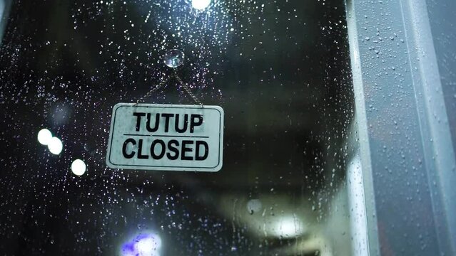 Open-closed board in the cafe pasted on the glass door at night and it's raining outside