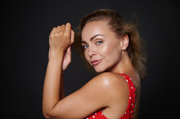 Portrait of a beautiful middle aged Caucasian woman with natural makeup and healthy glowing tanned skin, shiny flying blond hair, wearing red swimsuit isolated over black background with copy space