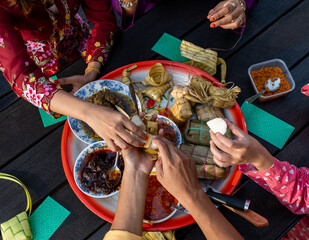Top View Hands of Muslim family enjoying a variety of traditional food on circular tray at end of Ramadan, on black table - obrazy, fototapety, plakaty
